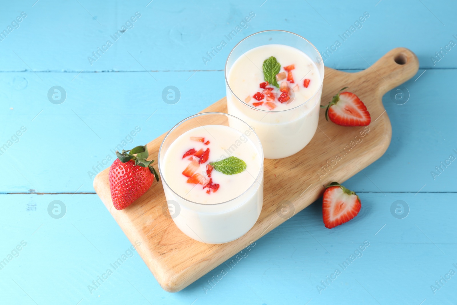 Photo of Tasty yogurt in glasses and strawberries on light blue wooden table