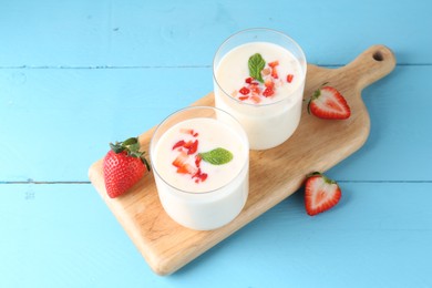 Photo of Tasty yogurt in glasses and strawberries on light blue wooden table