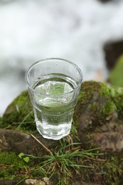 Photo of Glass of fresh water on stone with moss near stream, above view