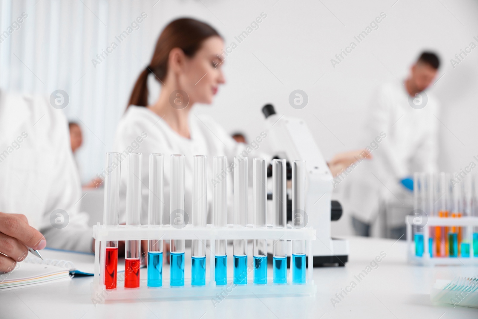 Photo of Rack with test tubes on white table and scientists in laboratory. Medical research