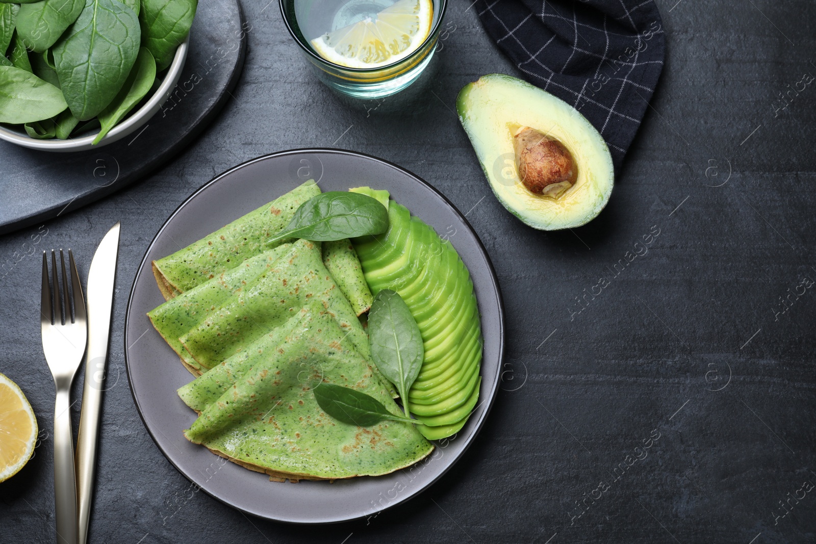 Photo of Delicious spinach crepes with avocado served on black table, flat lay