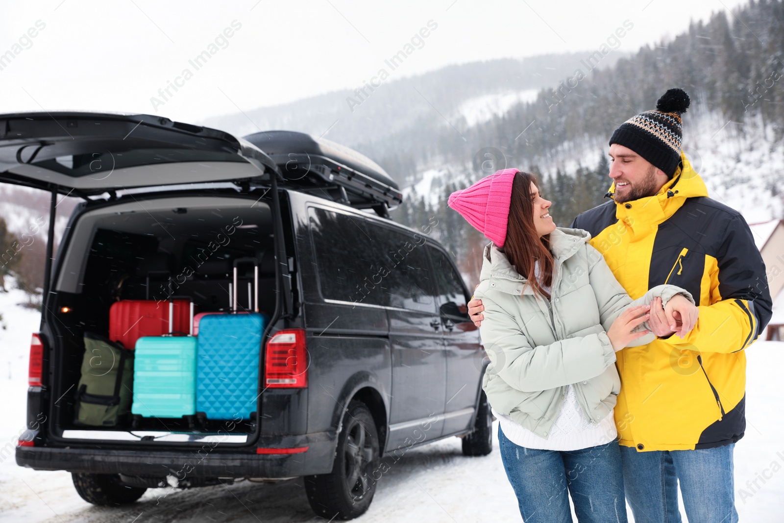 Photo of Happy couple near car with open trunk on snowy road. Winter vacation