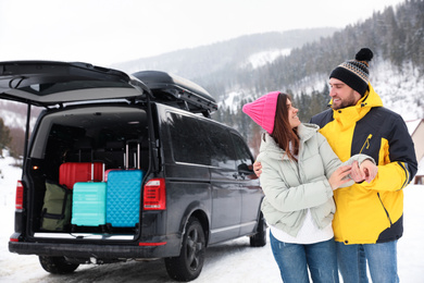 Happy couple near car with open trunk on snowy road. Winter vacation