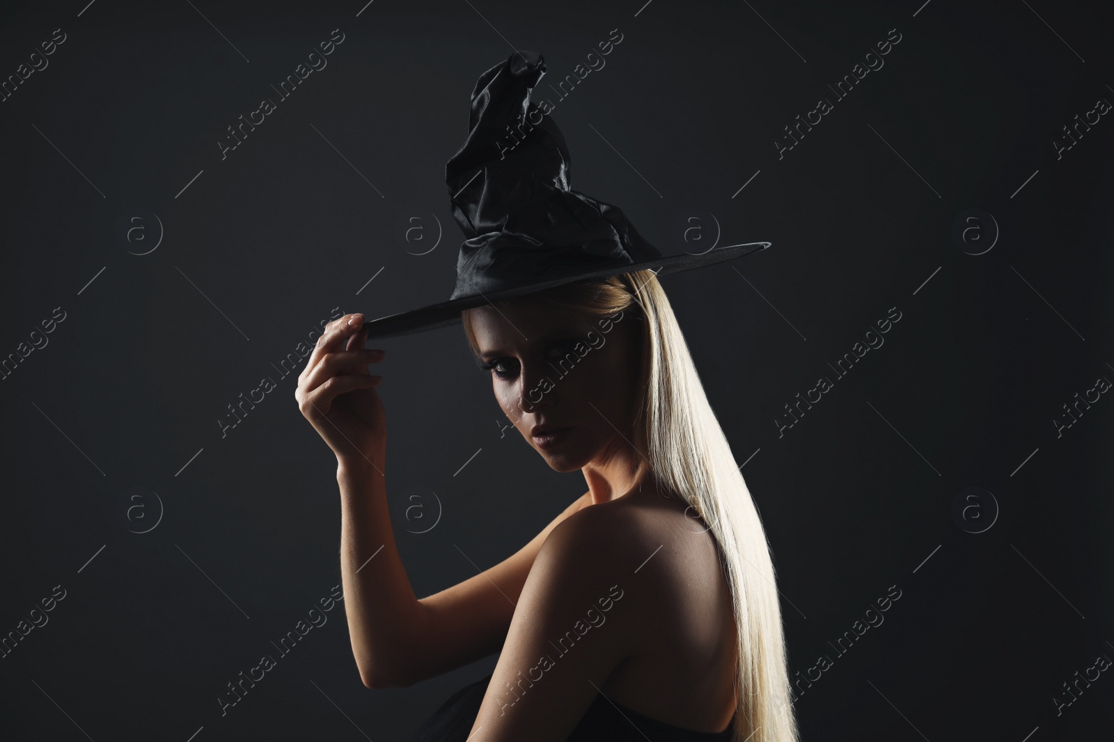 Photo of Witch in black hat on dark background. Scary fantasy character