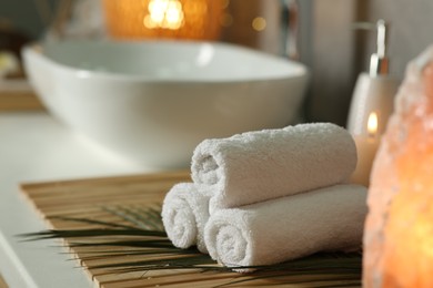 Photo of Spa composition. Rolled towels, burning candle and Himalayan salt lamp on countertop in bathroom, space for text