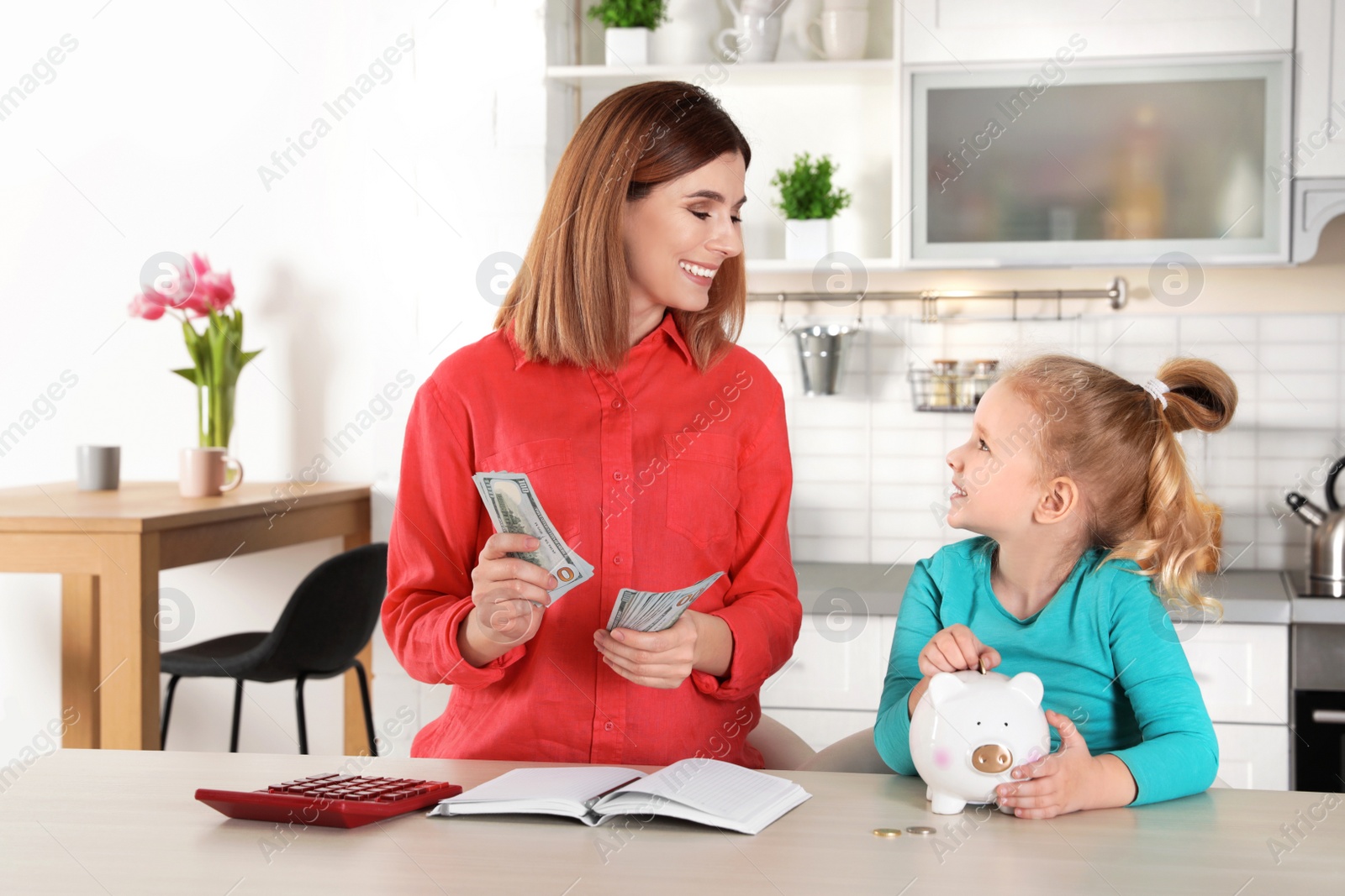 Photo of Mother and daughter with money at table in kitchen. Saving money