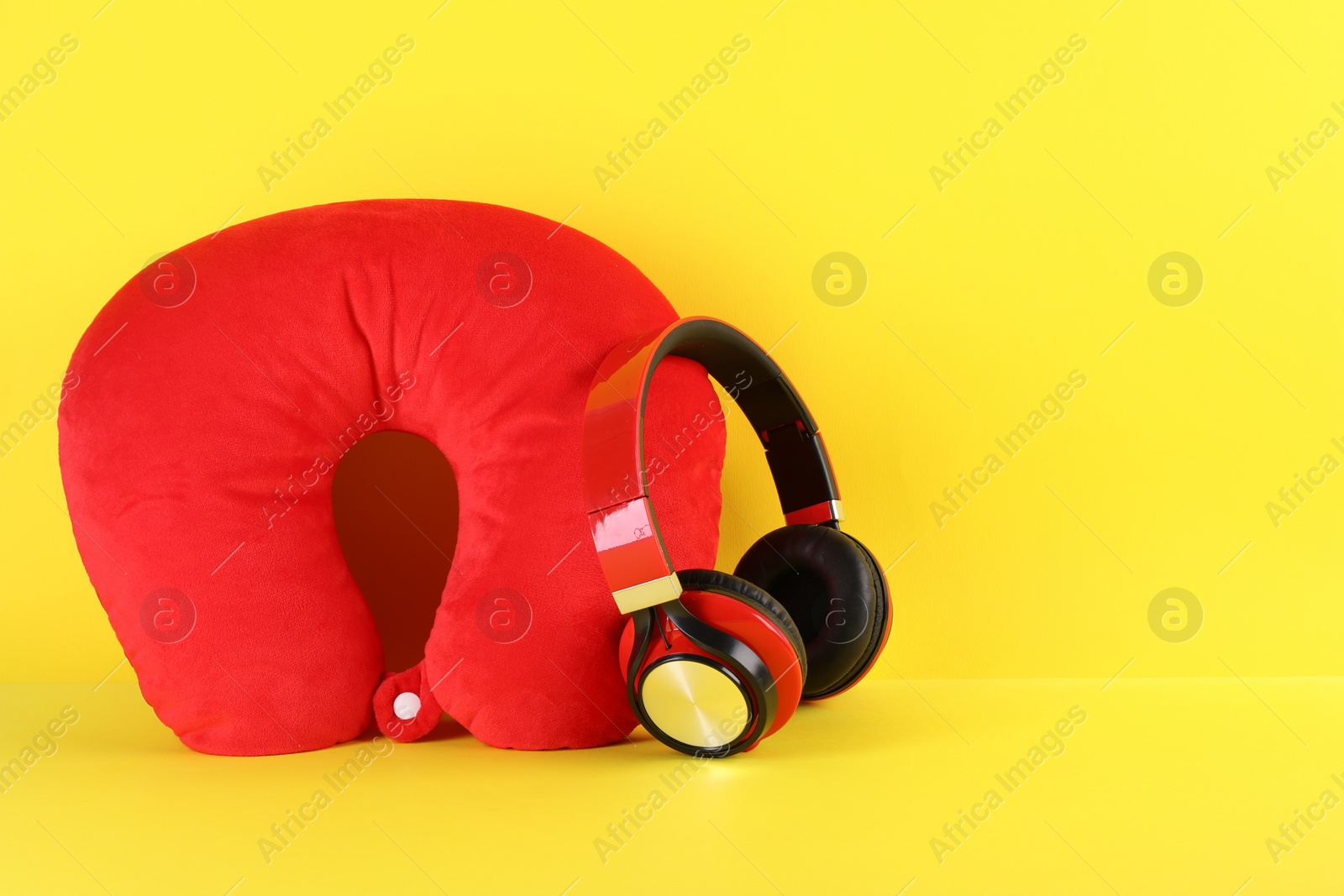 Photo of Red travel pillow and headphones on yellow background, space for text