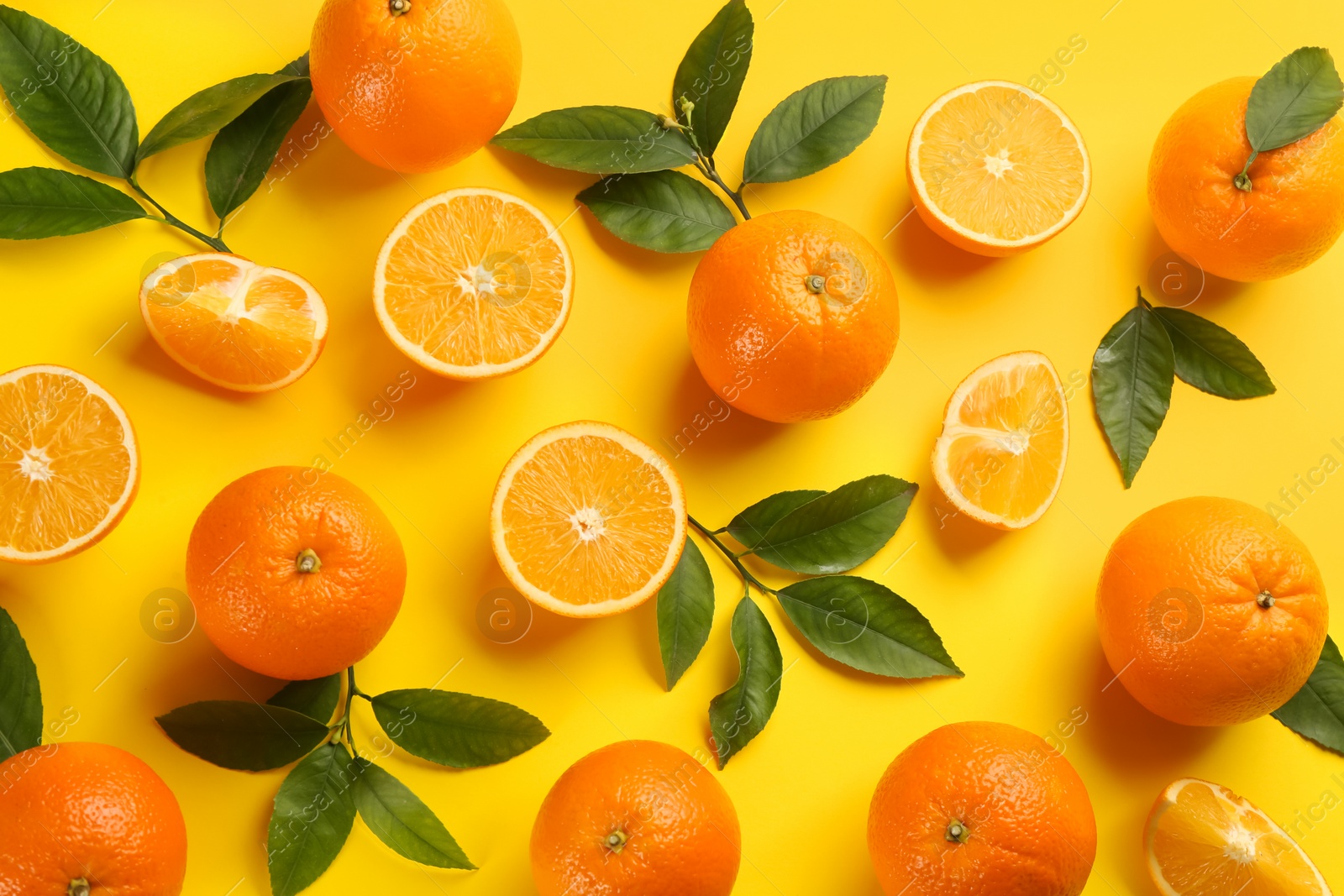 Photo of Fresh ripe oranges with green leaves on yellow background, flat lay