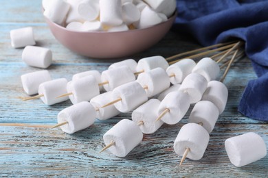 Photo of Sticks with delicious puffy marshmallows on light blue wooden table