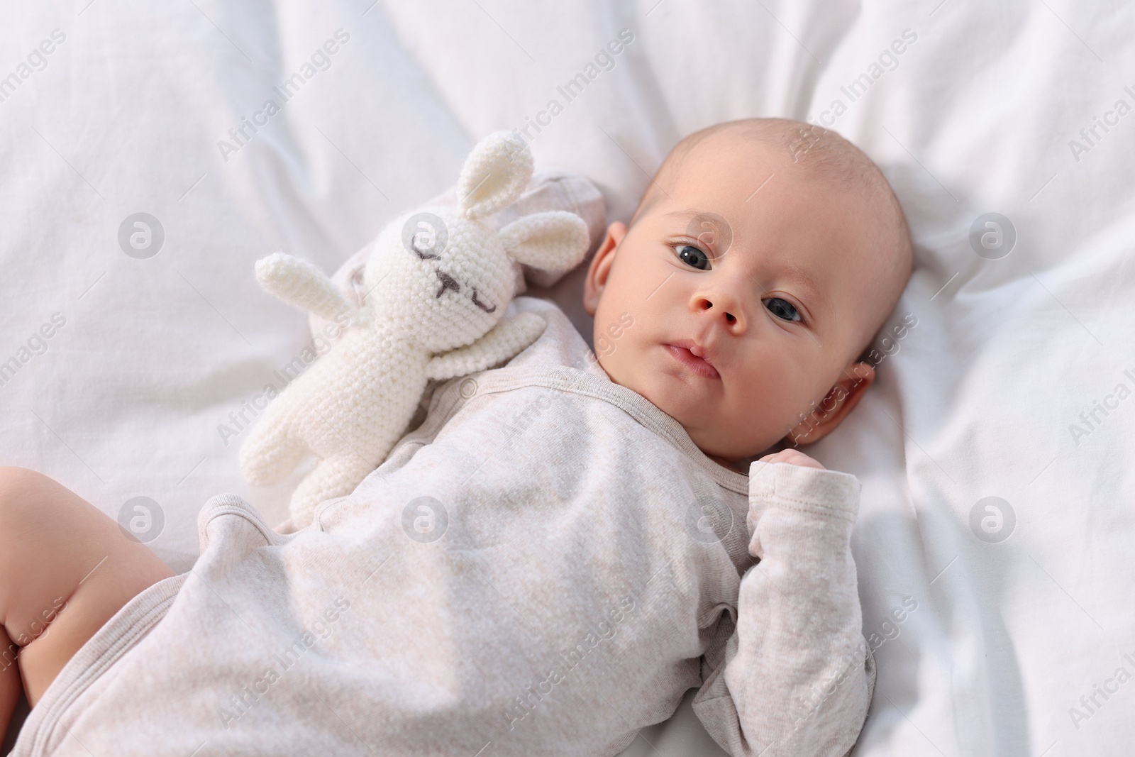 Photo of Cute little baby with toy lying on white sheets, top view