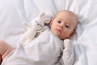 Photo of Cute little baby with toy lying on white sheets, top view