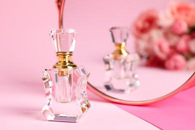 Photo of Bottle of perfume near mirror on pink background