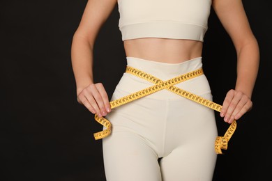 Photo of Woman in sportswear measuring waist with tape on black background, closeup