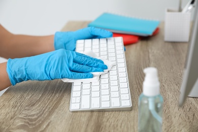 Photo of Woman cleaning computer keyboard with antiseptic wipe in office, closeup