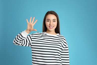 Photo of Woman showing number five with her hand on light blue background