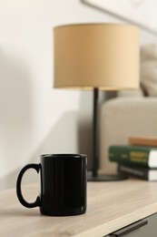 Black mug on wooden table indoors. Mockup for design