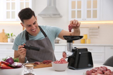 Photo of Man using modern meat grinder in kitchen