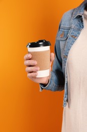 Woman holding takeaway cup with drink on orange background, closeup. Coffee to go