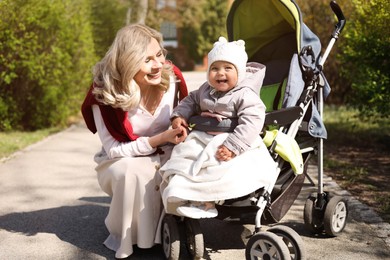 Photo of Happy mother with her daughter in stroller outdoors on sunny day