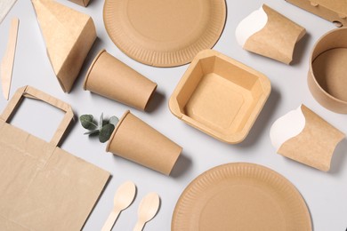 Photo of Eco friendly food packaging. Paper containers, tableware and eucalyptus leaves on light grey background, above view