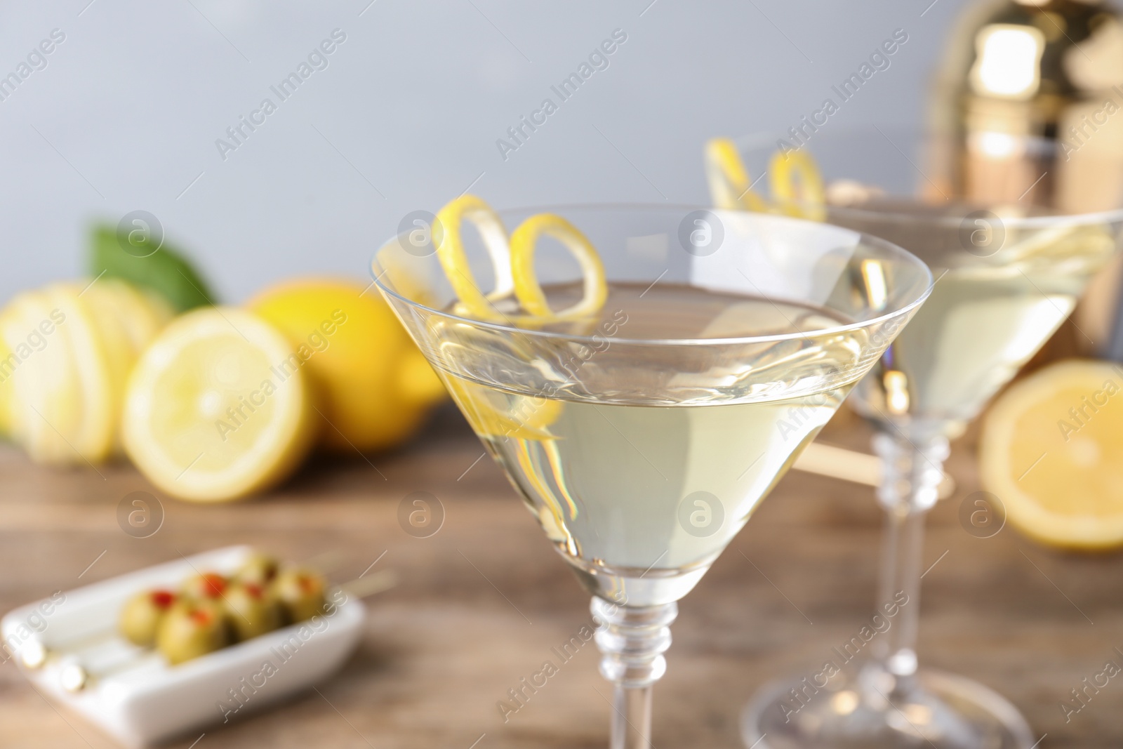 Photo of Glasses of lemon drop martini cocktail with zest on wooden table against grey background