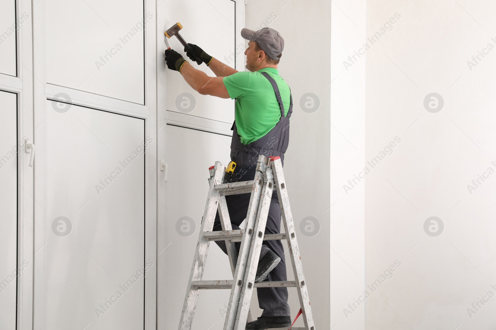 Photo of Worker on folding ladder installing window indoors