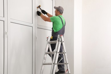 Photo of Worker on folding ladder installing window indoors