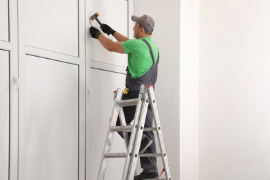 Worker on folding ladder installing window indoors