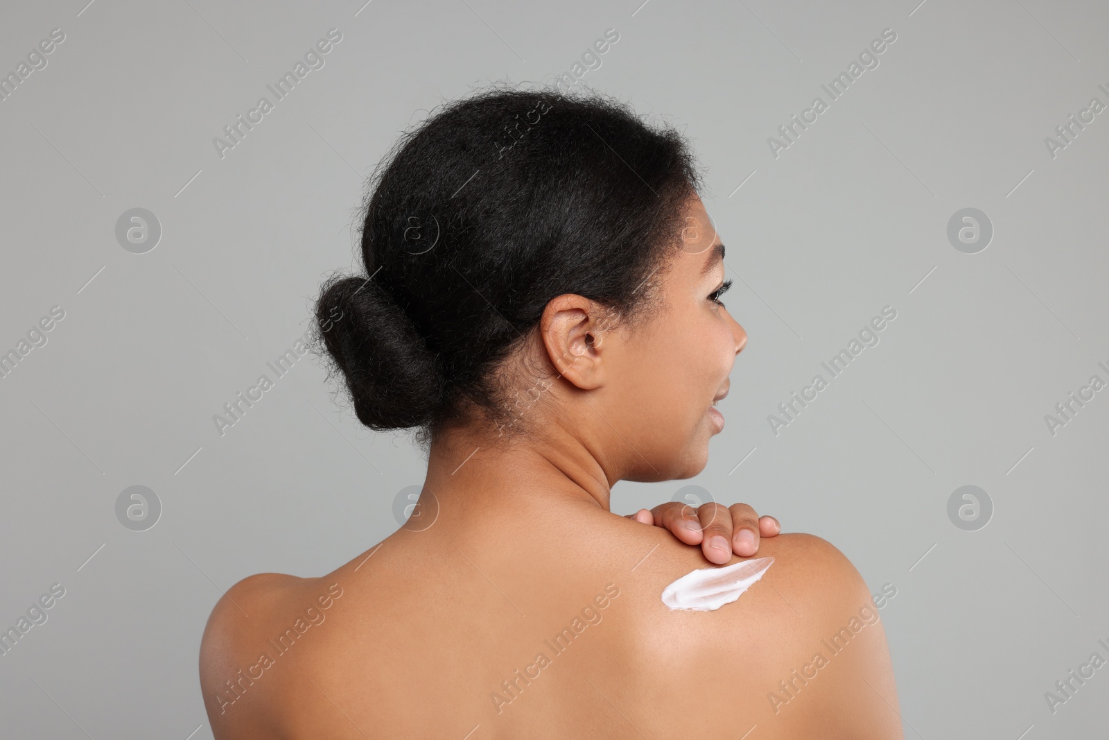 Photo of Young woman applying body cream onto back on grey background