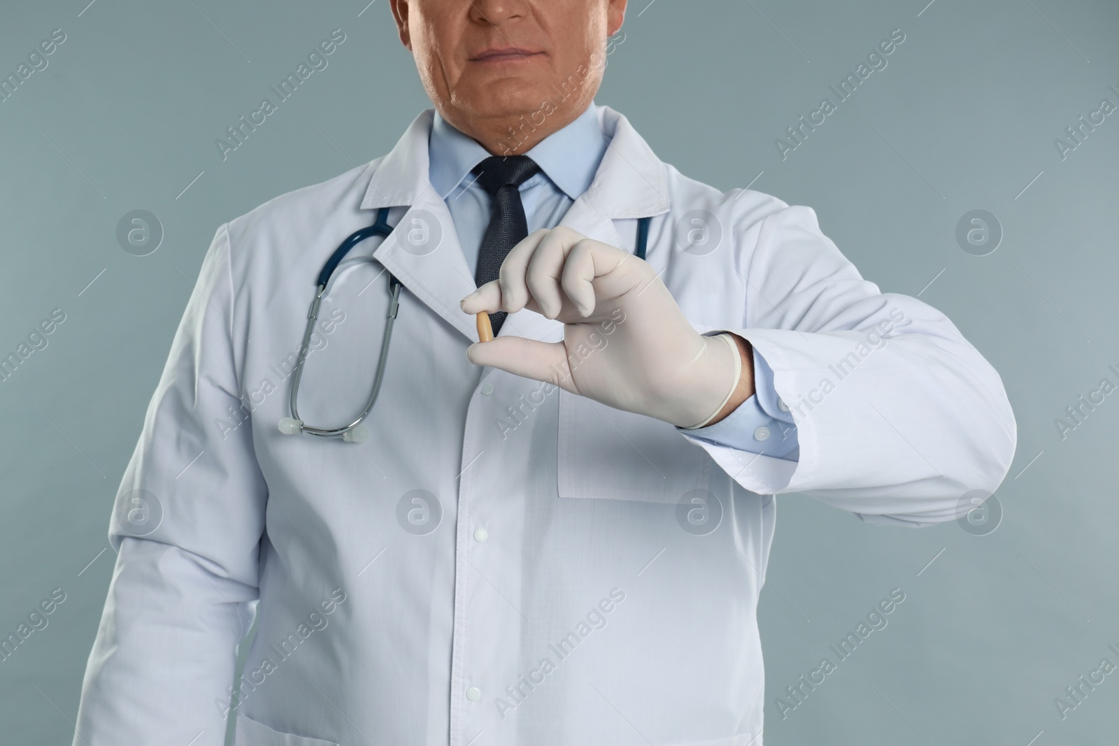 Photo of Doctor holding suppository for hemorrhoid treatment on light grey background, closeup