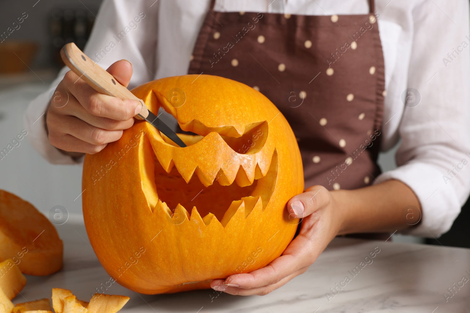 Photo of Woman carving pumpkin for Halloween at white marble table, closeup