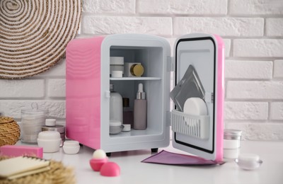 Photo of Mini fridge with cosmetic products on white vanity table