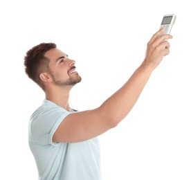 Photo of Happy young man operating air conditioner with remote control on white background