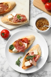 Photo of Delicious bruschettas with prosciutto served on marble table, flat lay