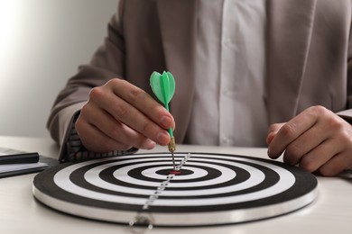 Business targeting concept. Man with dart aiming at dartboard at table indoors, closeup