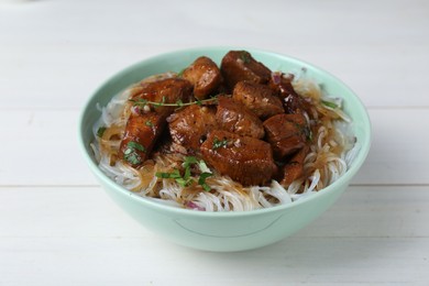 Photo of Bowl with pieces of soy sauce chicken and noodle on white wooden table, closeup