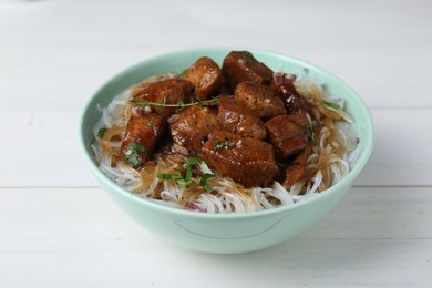 Bowl with pieces of soy sauce chicken and noodle on white wooden table, closeup