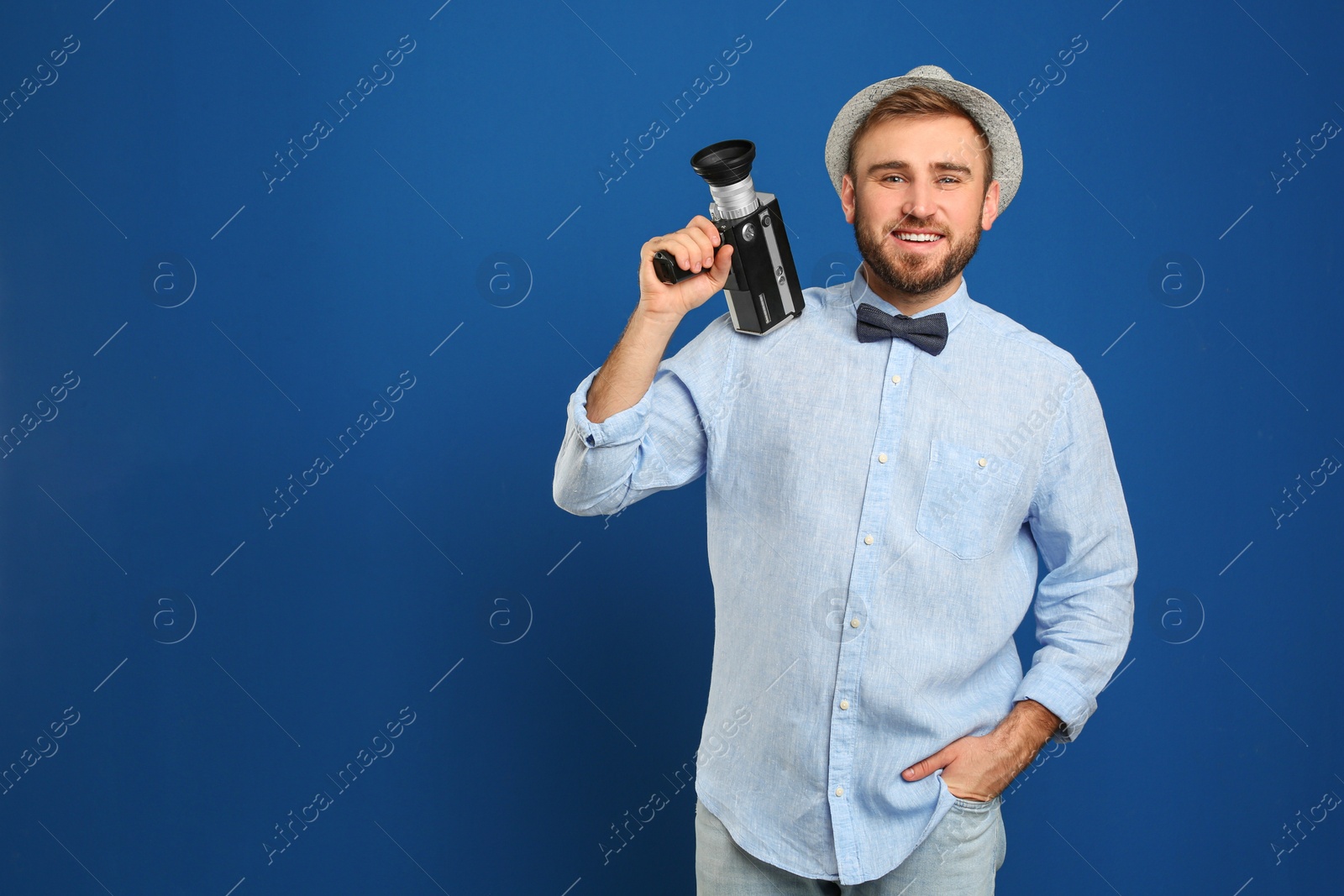 Photo of Young man with vintage video camera on blue background. Space for text