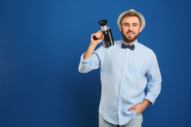 Young man with vintage video camera on blue background. Space for text