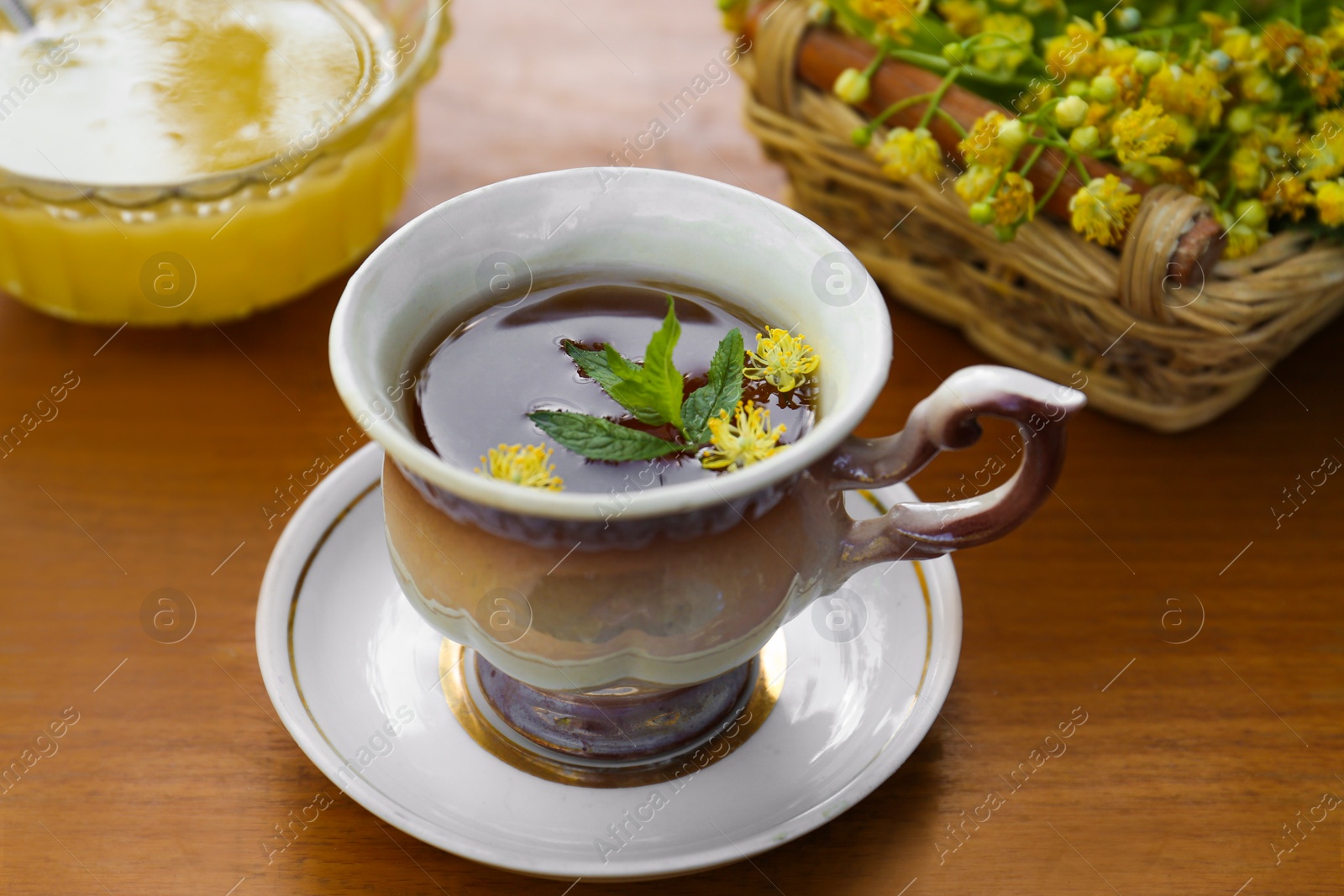 Photo of Cup of hot aromatic herbal tea, honey and linden blossoms on wooden table, closeup