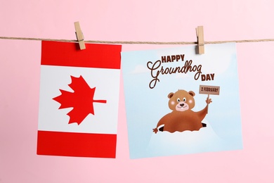 Photo of Happy Groundhog Day greeting card and Canada flag hanging on pink background