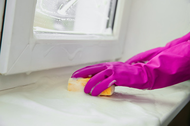 Photo of Woman cleaning window sill with sponge indoors, closeup