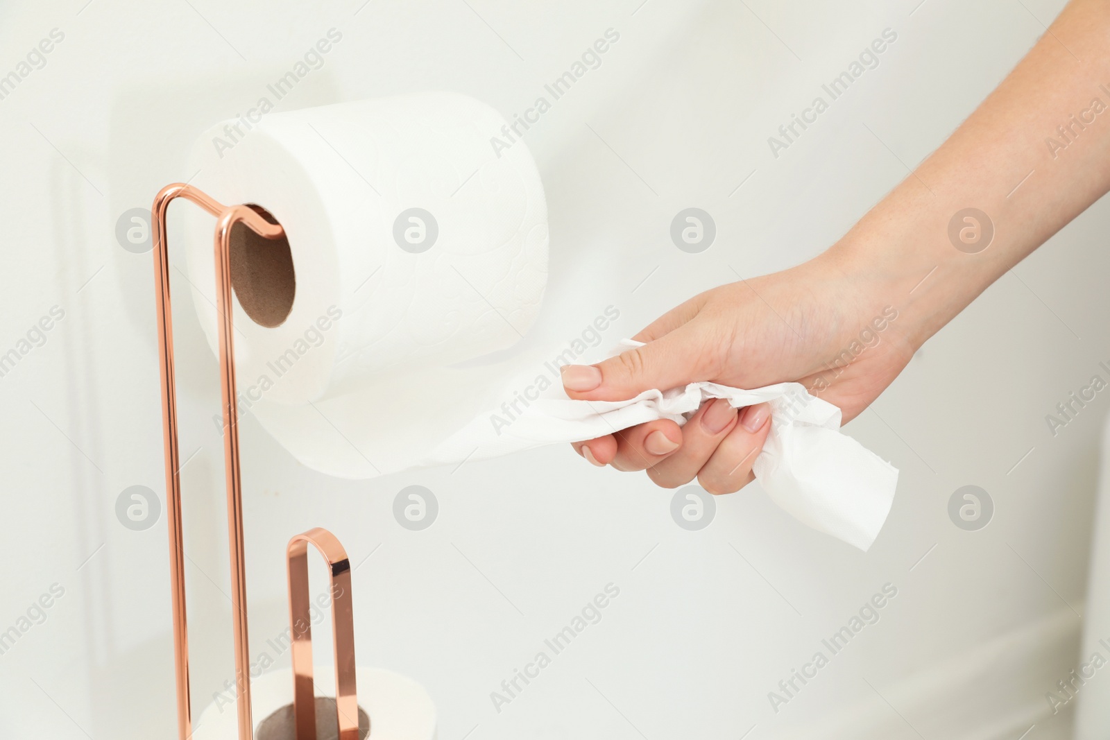 Photo of Woman taking toilet paper from roll holder in bathroom, closeup