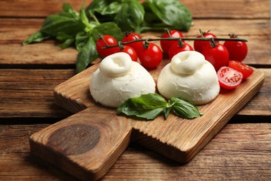 Photo of Delicious burrata cheese with basil and cherry tomatoes on wooden table