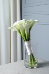 Beautiful calla lily flowers in glass vase on light grey table indoors