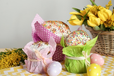 Photo of Delicious Easter cakes, dyed eggs and basket with flowers on table