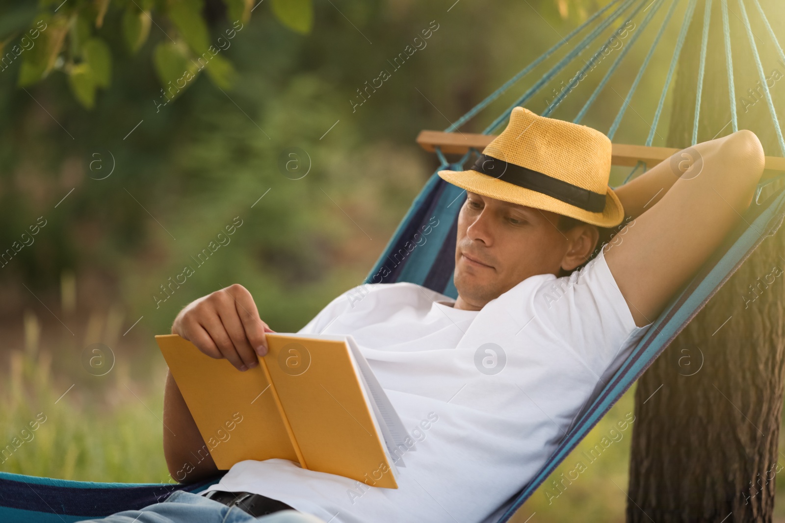 Photo of Man reading book in comfortable hammock at green garden