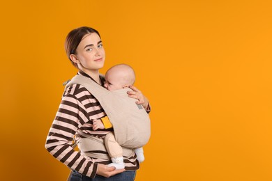 Mother holding her child in sling (baby carrier) on orange background. Space for text