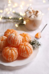 Photo of Peeled delicious ripe tangerines and glass of drink with marshmallows on white bedsheet