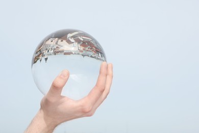 View of beautiful city street, overturned reflection. Man holding crystal ball against sky, closeup. Space for text